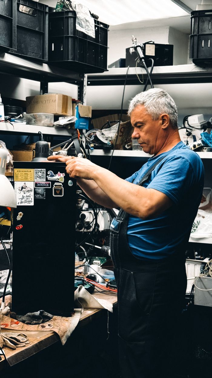 Senior man repairing equipment in a cluttered workshop filled with tools.