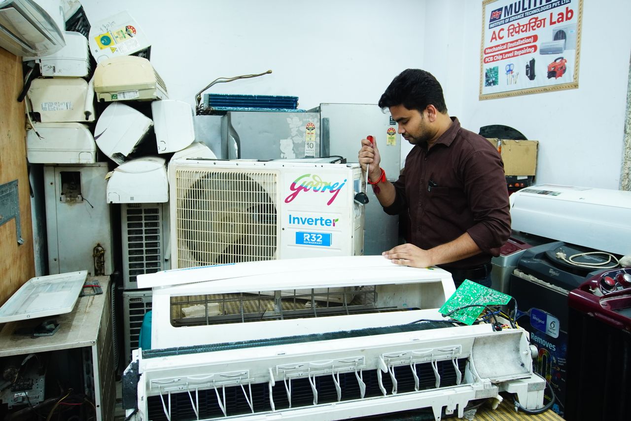 services-01 Technician repairing an air conditioner unit in New Delhi workshop.