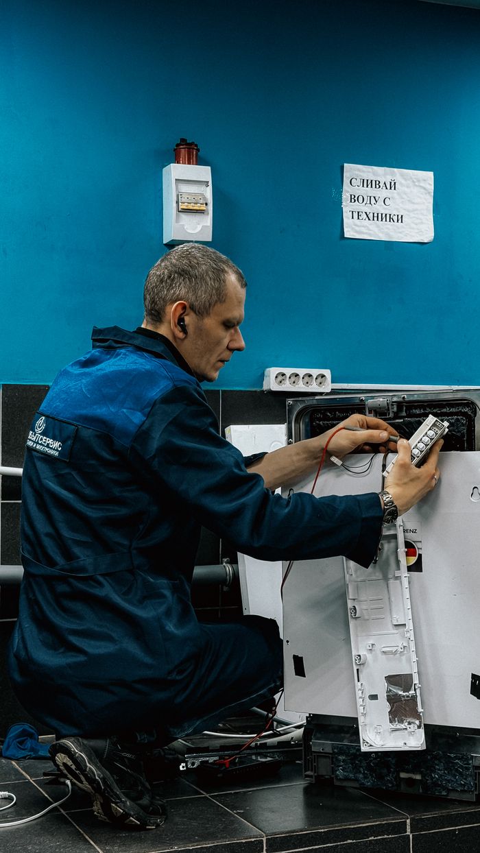 about-02 A focused technician in blue uniform repairs a home appliance in an indoor setting.