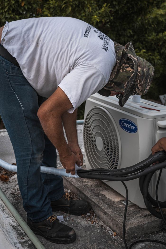 why-choose-us-03 A technician performs maintenance on an outdoor air conditioning unit, focusing on hose connections.